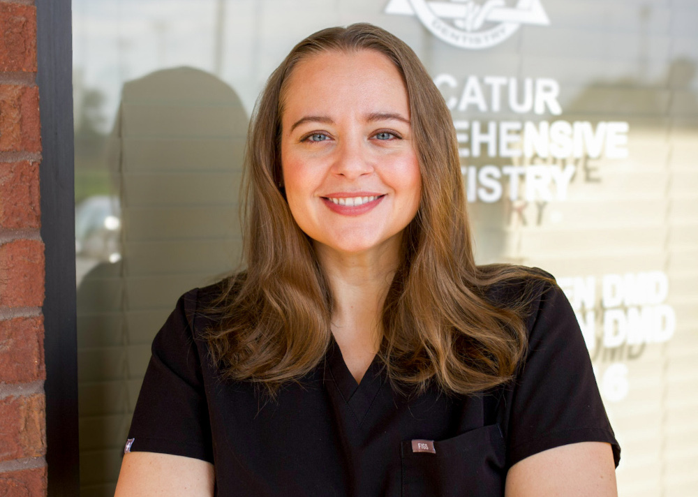 Dr. Kimberly Welden, DMD, in black scrubs smiling outside the Decatur Comprehensive Dentistry office window in Decatur, AL