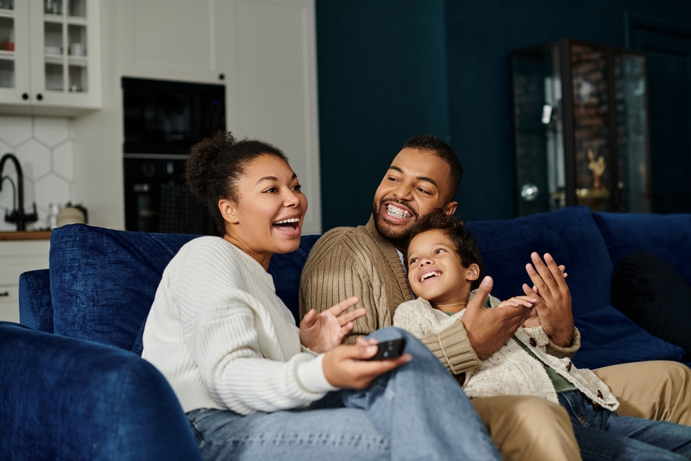 Smiling family relaxing on a blue couch at home, father wearing braces, representing family dental care in Decatur, AL